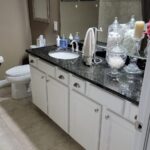A bathroom with white cabinets and granite countertops, featuring sleek tiling.