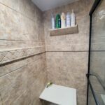 A tiled shower with a shelf for storage and soap dispenser.