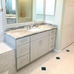 A bathroom with white cabinets and marble countertops underwent a remodel.