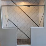 A glass shower door in a bathroom with tiling.