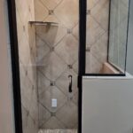 A modern shower with a glass door and tiled floor.