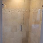 A bathroom with a glass shower door and beige tiling.