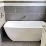 A white bathtub in a gray tiled bathroom.