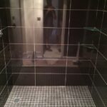 A black tiled shower with a person standing in it.