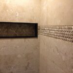 A shower with a beige tiled wall in the bathroom.
