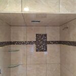 A shower with beige tile and a glass shelf in a bathroom remodel.