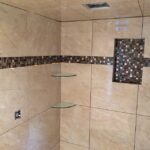 A shower with beige tile and glass shelves for a bathroom remodel.