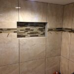 A tiled shower with a beige tiled wall in the bathroom.