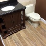 A bathroom with a toilet and a sink underwent remodeling, which included new tiling and a cabinet installation.