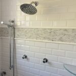 A white tiled bathroom with a glass shower head.