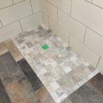 A tiled shower with green on the floor.