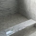 A gray tiled bathroom with a marble floor.