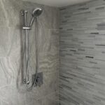 A shower with a grey tiled wall and shower head in the bathroom.