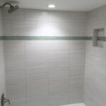 A white tiled shower with a green floor.