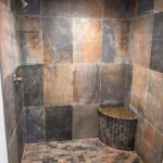 A shower with brown tiling and a granite bench.