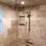 A tiled shower with a beige shower head in a bathroom remodel.