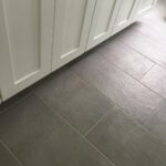 A grey tile floor in a bathroom with white cabinets.