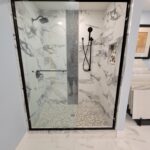 A bathroom with a glass shower door and marble tiling.