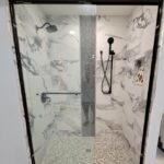 A black and white shower with a glass door in a bathroom remodel.