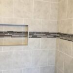 A tiled shower with a shelf and walls.