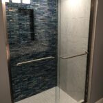 A bathroom with a glass shower door and blue tile.