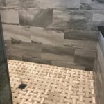 A tiled shower with a tiled floor in the bathroom remodel.