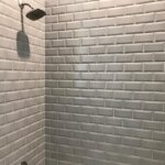A white tiled shower with a shower head.