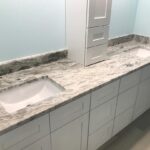 A bathroom with white cabinets and granite counter tops underwent a remodel with new tiling.