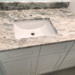 A remodeled bathroom with a white sink and marble counter top.