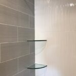 A bathroom with tiled walls and a glass shelf.