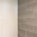 A bathroom with a grey tiled wall and a shower.