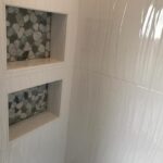 A white tiled shower with a shelf.