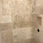 A beige tiled shower with a matching floor in a bathroom remodel.