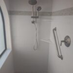 A shower with a hand rail and a window in the bathroom.