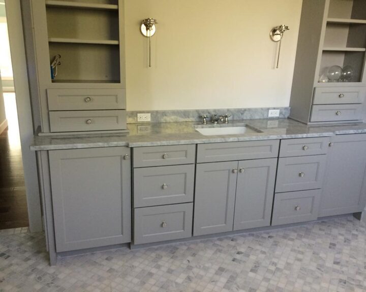 A bathroom with gray cabinets and marble countertops.