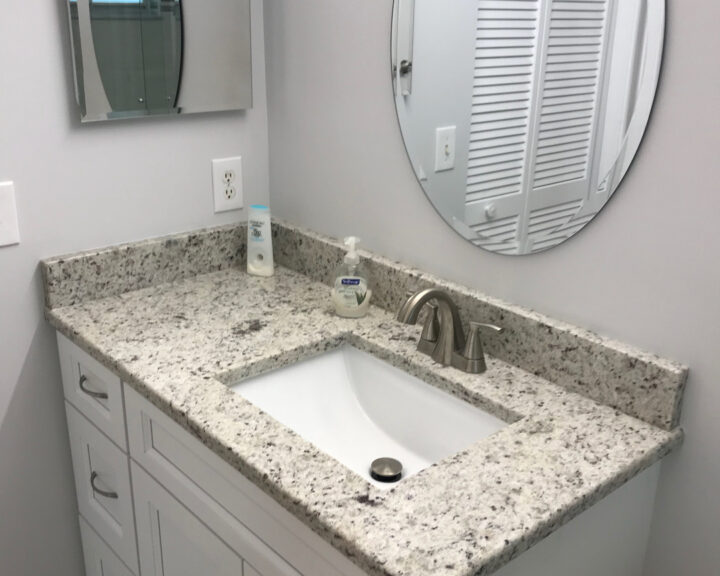 A bathroom with granite counter tops and a mirror.