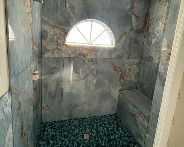 A shower with a blue tile floor and a window in the bathroom.